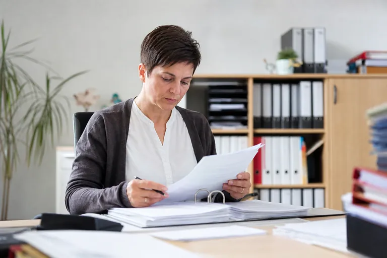 Pflegedienstleitung arbeitet mit Gesetzestext und Prüfunterlagen am Schreibtisch.